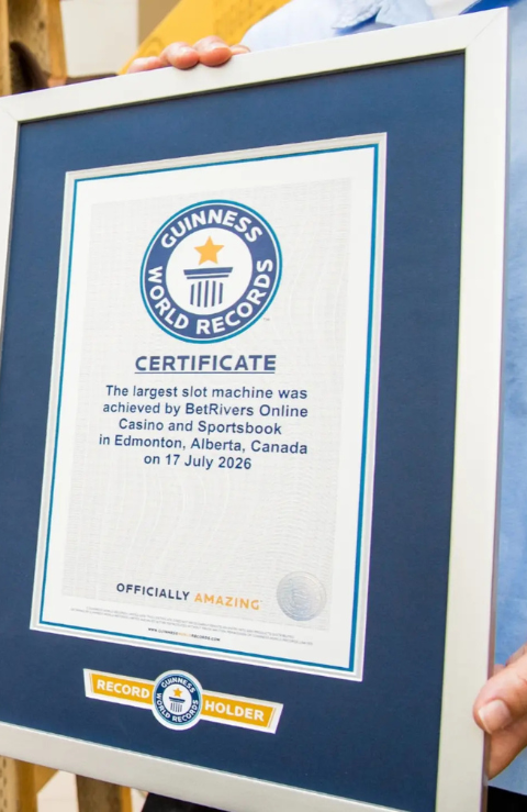 The biggest slot » GP Framed Guinness World Records certificate being held up by a person, shown on a dark blue matting surface.