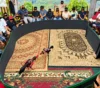 Crowd gathered around a circular cockfighting ring as two roosters spar on ornate carpets inside the arena.