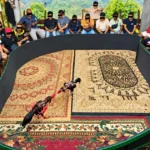 Crowd gathered around a circular cockfighting ring as two roosters spar on ornate carpets inside the arena.